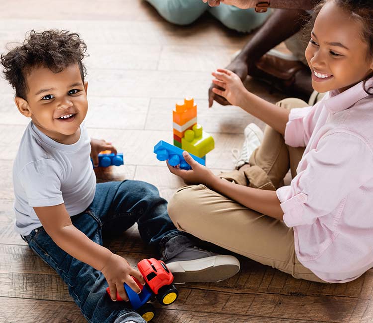 View of african american brother and sister playing with toy truck and building blocks on floor at home