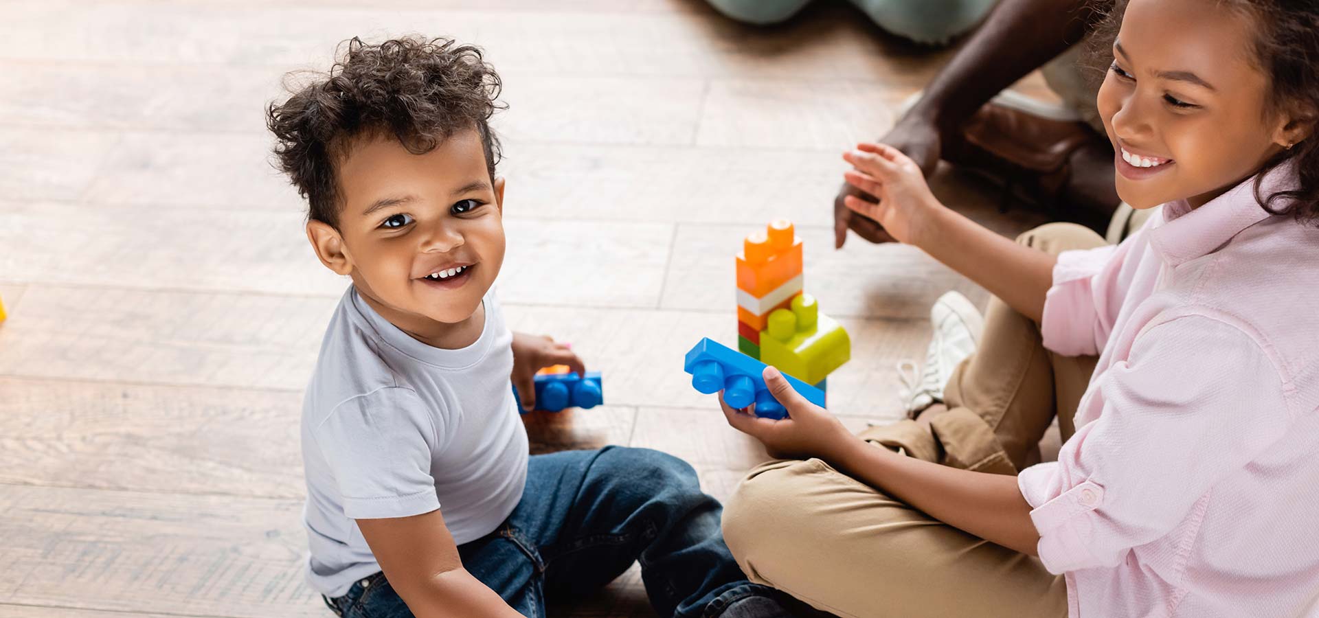 View of african american brother and sister playing with toy truck and building blocks on floor at home